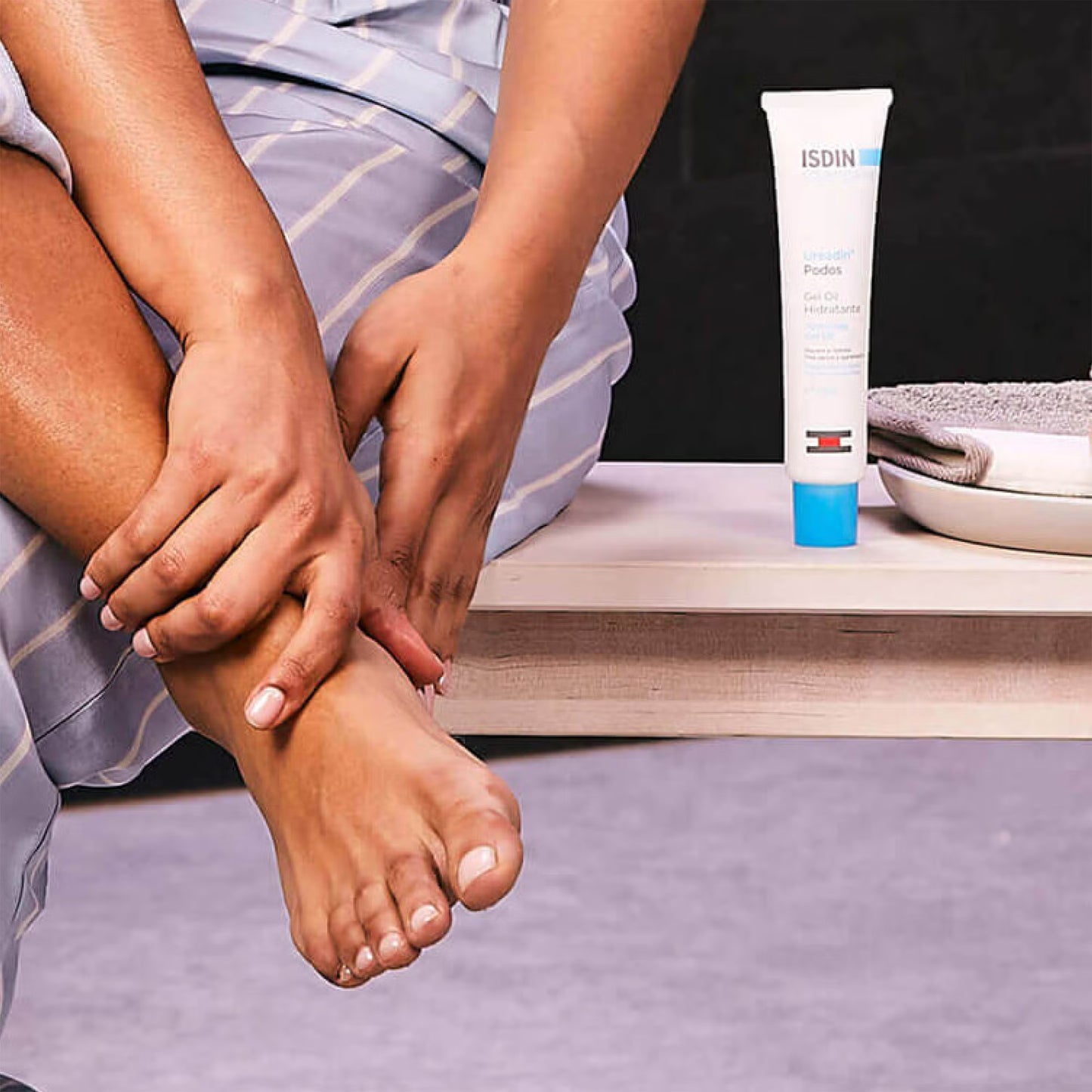 Person applying cream to their foot with a tube of Isdin cream in the background.