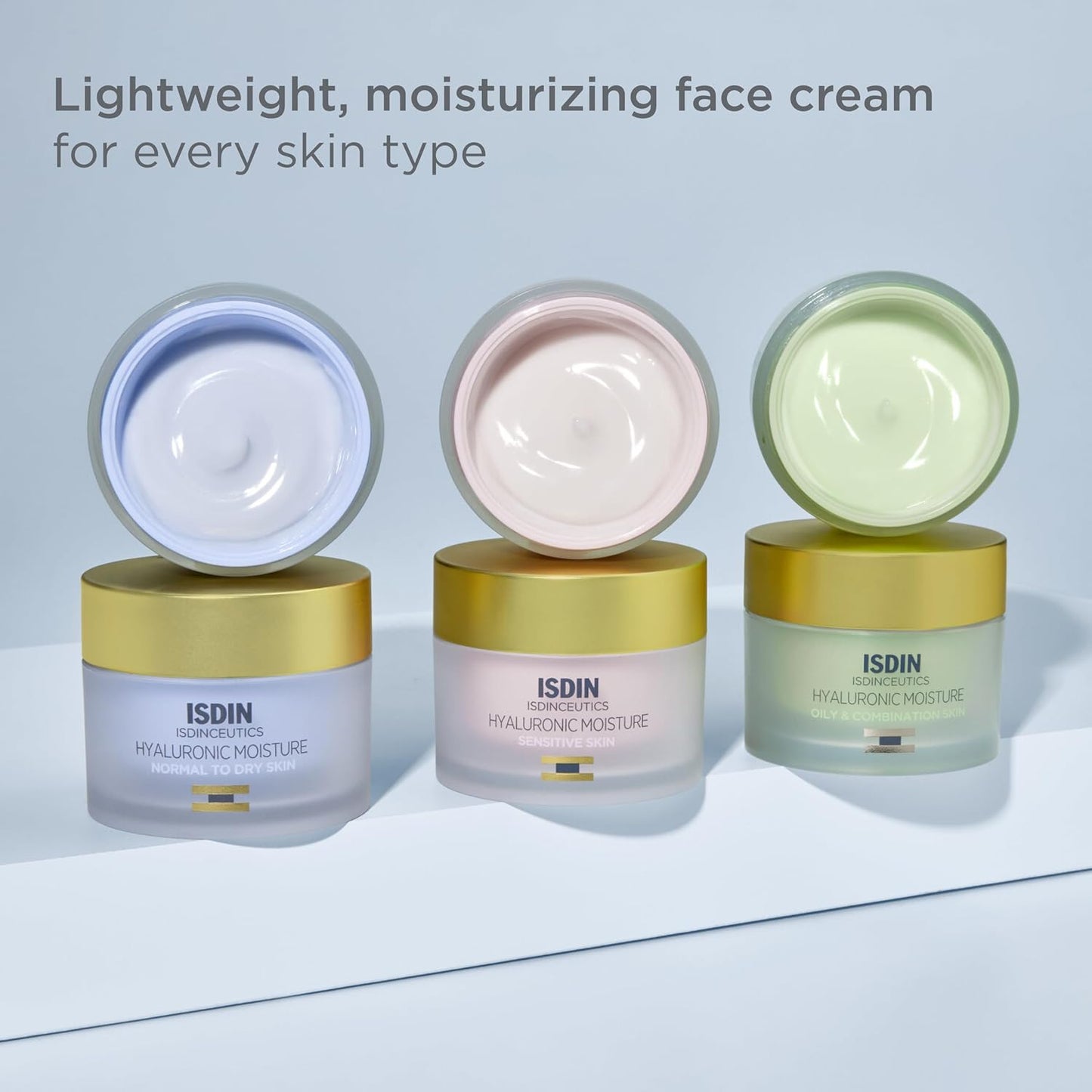 Three open jars of ISDIN moisturizing face cream on a light blue background