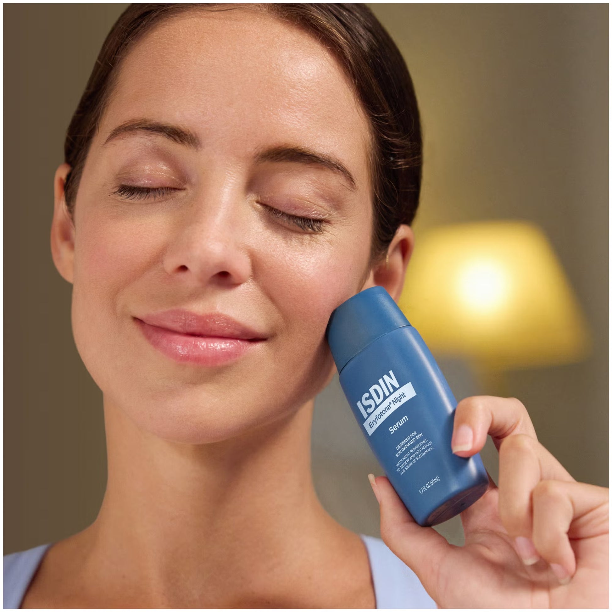 Woman holding a blue ISDIN serum bottle near her face with a blurred background