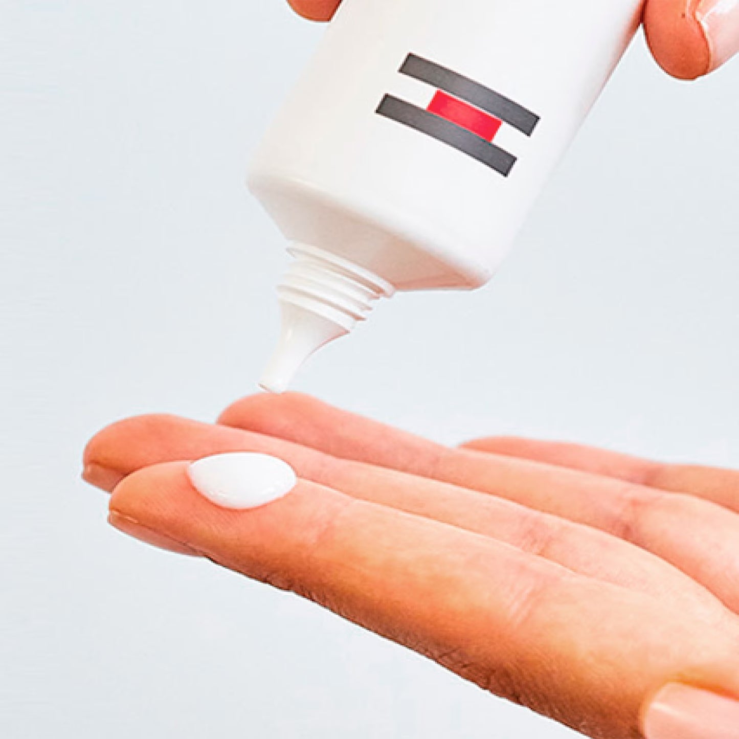 Hand holding a small white object with a bottle in the background