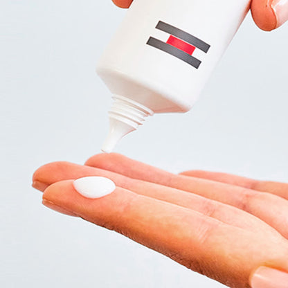 Hand holding a small white object with a bottle in the background