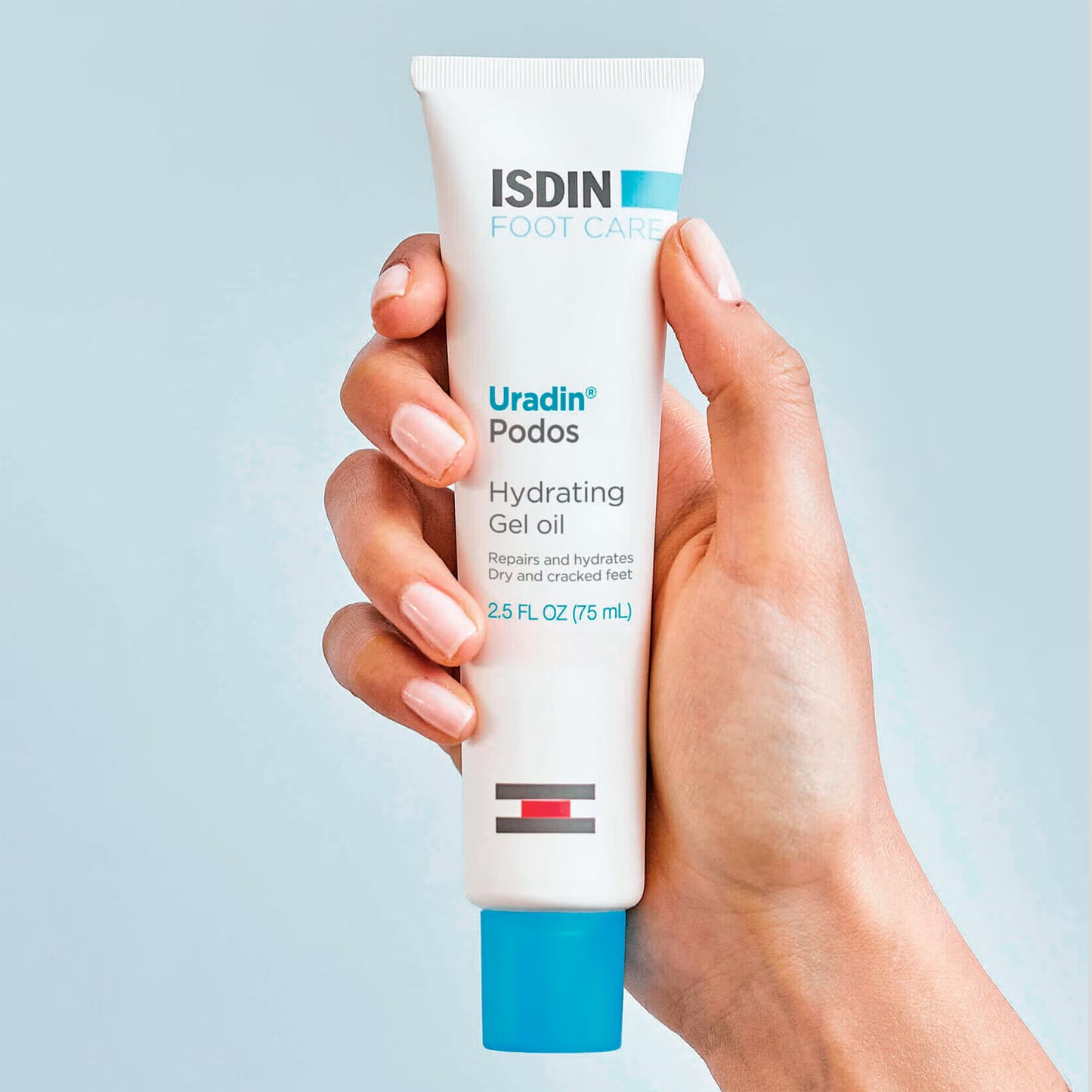 Hand holding a tube of ISDIN Uradin Podos Hydrating Gel Oil against a light blue background