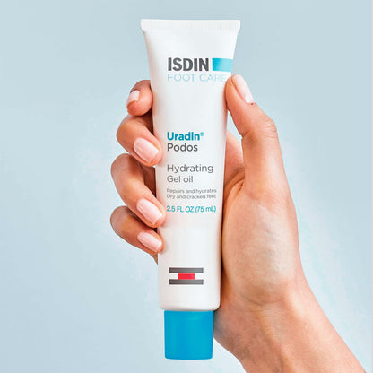 Hand holding a tube of ISDIN Uradin Podos Hydrating Gel Oil against a light blue background