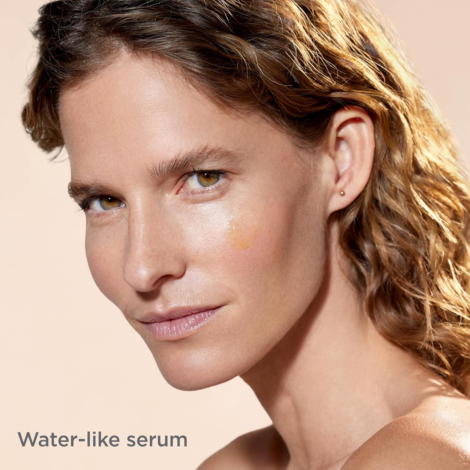 Woman with a water-like serum applied to her face on a beige background