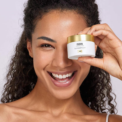 Woman holding Isdin skincare product close to her face against a plain background
