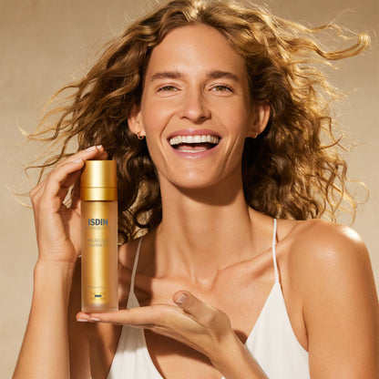 Woman holding a skincare product with ISDIN branding against a beige background