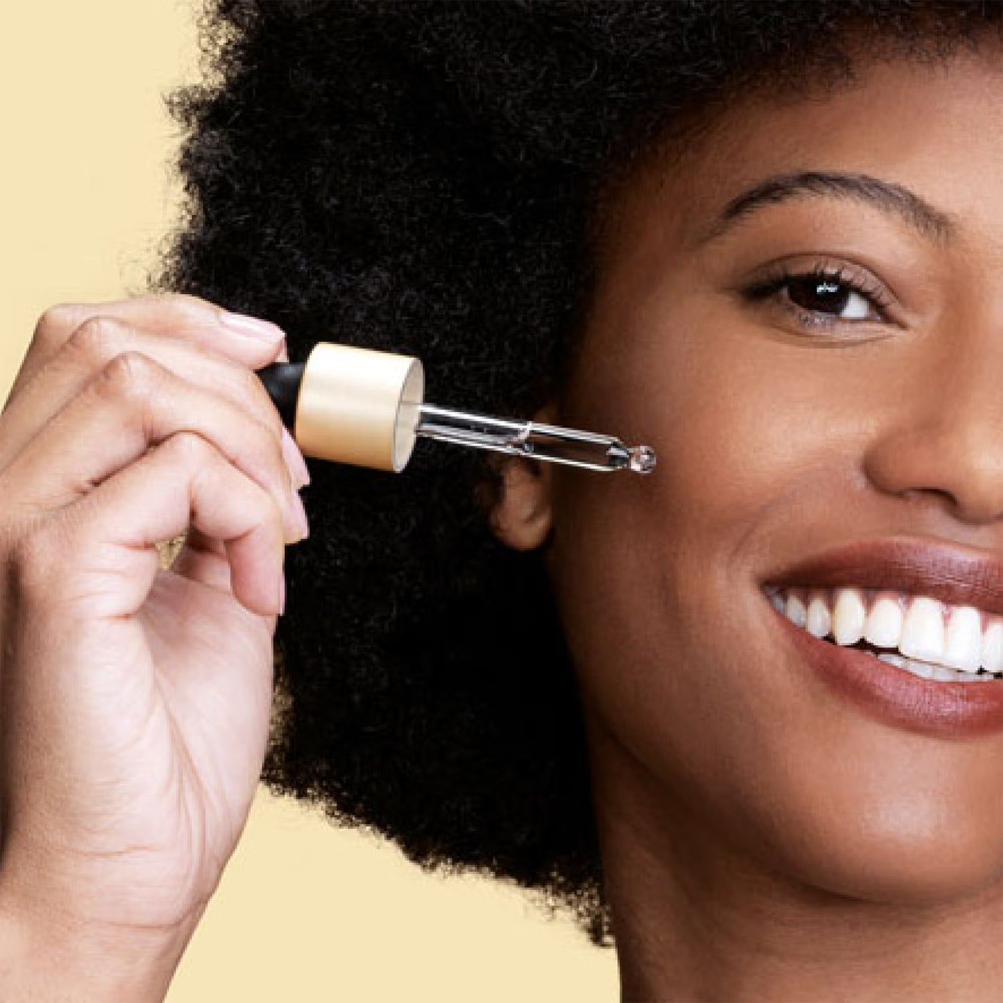 Woman applying skincare product to her face with a dropper against a beige background