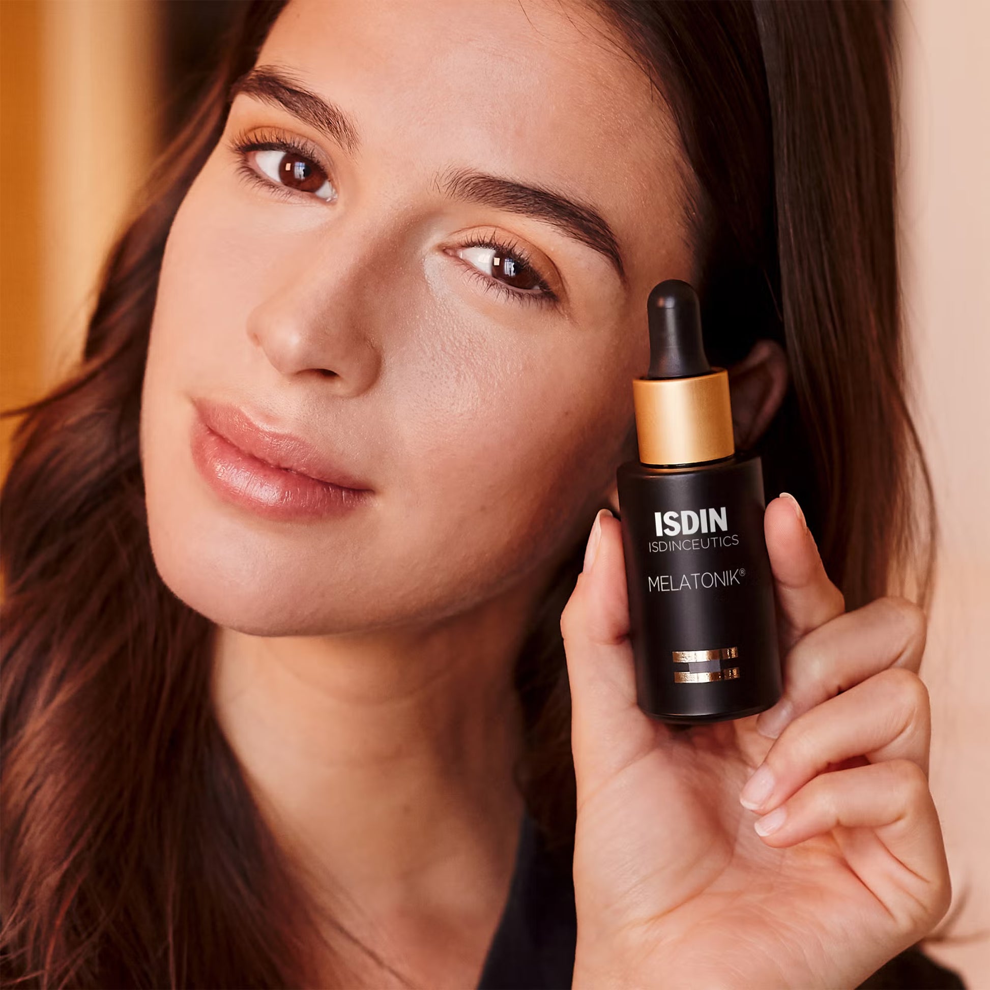 Woman holding ISDIN Melatonik skincare dropper bottle close to her face.