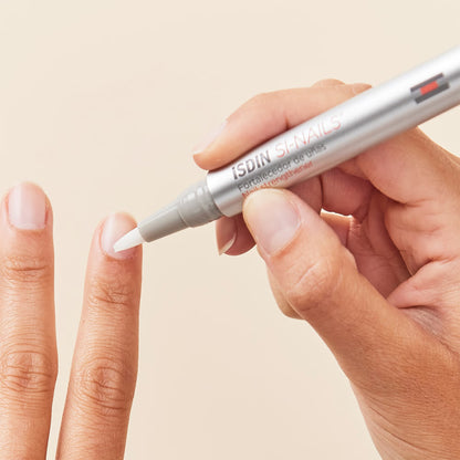 Hand holding a silver pen with 'ISDIN' branding, applying a product to a finger on a beige background