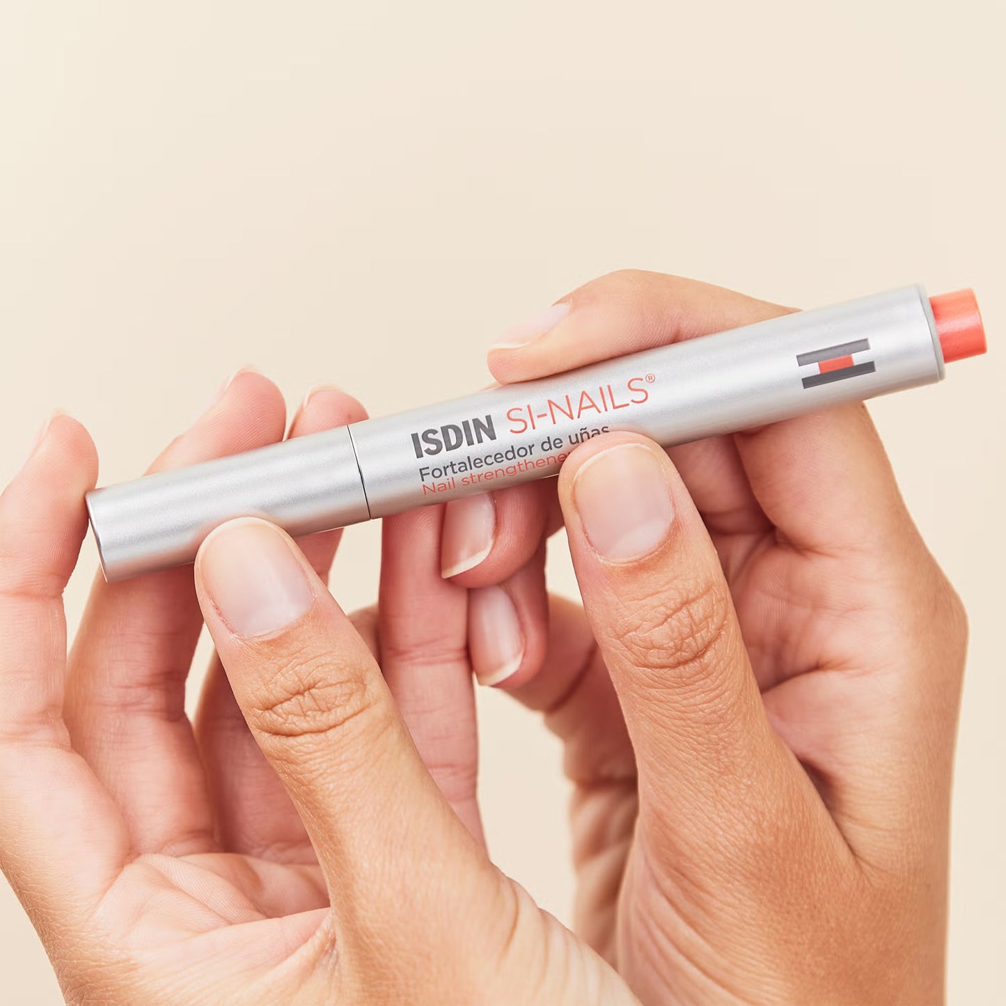 Hand holding a silver and red ISDIN SI-NAILS product against a beige background